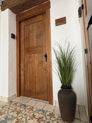 A wooden door with a nameplate, a potted plant, and a tiled floor. - The Jewel of Setenil - Zafiro Cave House (Setenil de las Bodegas)