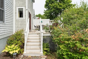 A residential property with a front porch, a white picket fence, and a variety of shrubs and trees. - Northeast Harbor Hideaway | Walk to the waterfront (Mount Desert)
