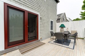 A covered patio with a table and chairs, a sliding glass door, and a white picket fence. - Northeast Harbor Hideaway | Walk to the waterfront (Mount Desert)