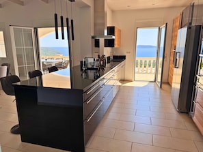 Una cuina moderna amb una illa gran, portes corredisses de vidre que donen a un balcó amb vistes al mar.