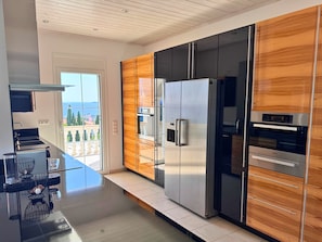 A modern kitchen with a stainless steel refrigerator, built-in oven, and wooden cabinetry. - Villa Mandola, exclusive dream villa with pool and sea views in Finikounda (Grizokampos)
