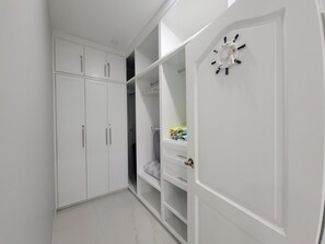 A white walk-in closet with multiple shelves and a clock on the door.