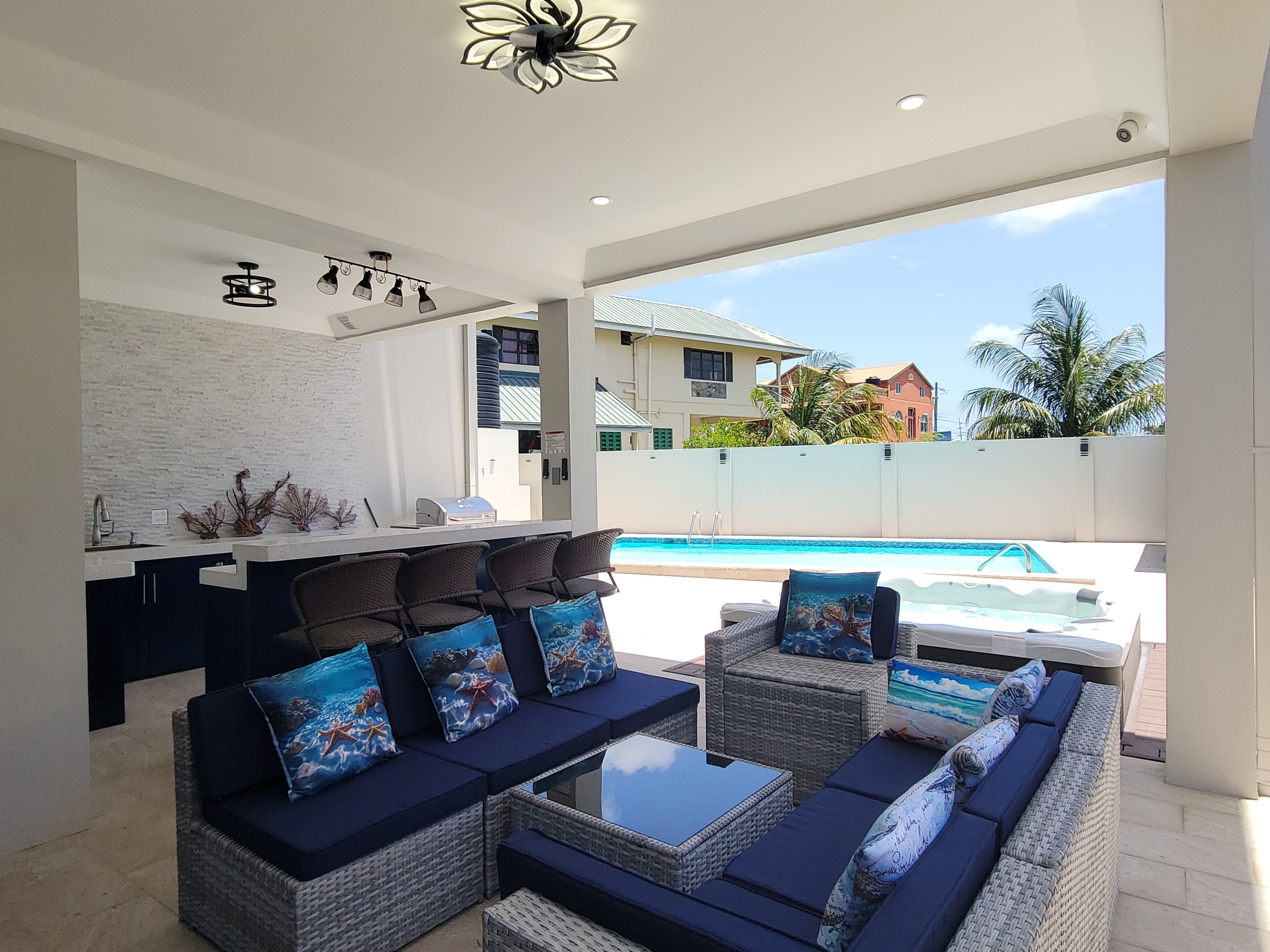 A modern outdoor seating area with wicker furniture and cushions, a pool, and a view of a residential building.