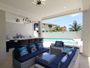 A modern outdoor seating area with wicker furniture and cushions, a pool, and a view of a residential building.