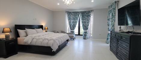 Quarto com cama, mesas de cabeceira, cômoda, televisão e lustre.