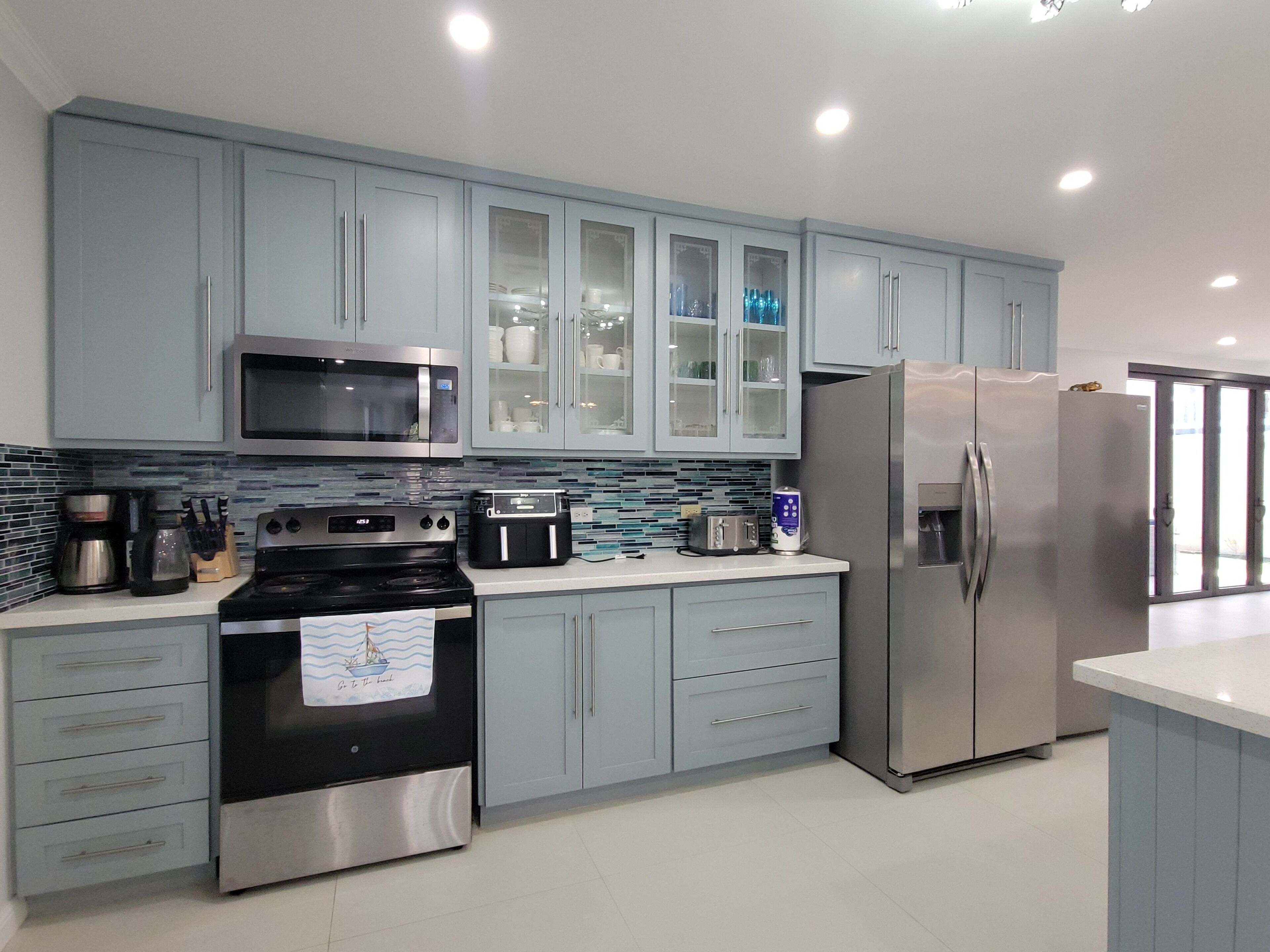 A modern kitchen with stainless steel appliances, light blue cabinetry, and a tiled backsplash.