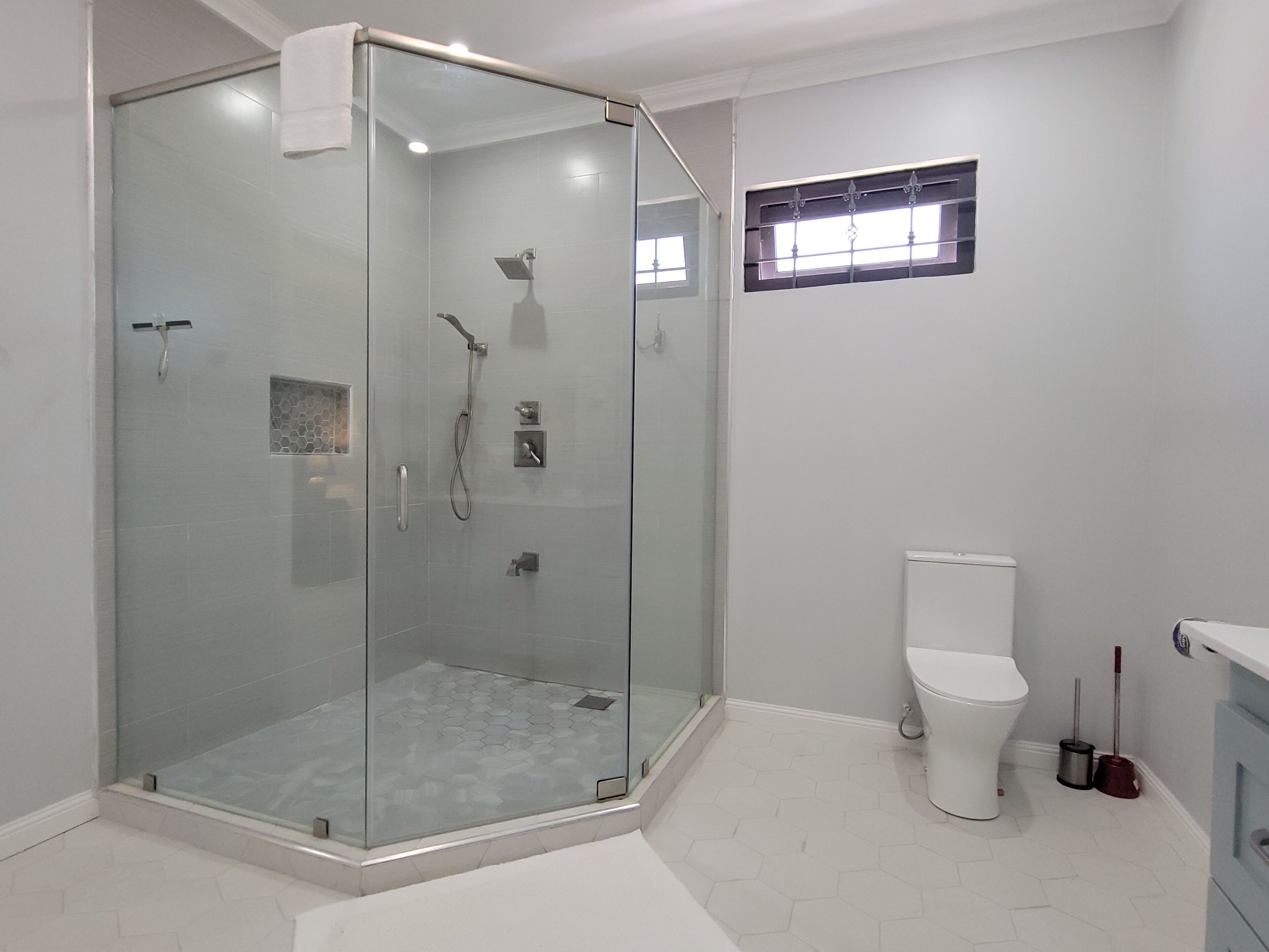 A modern bathroom with a glass-enclosed shower, a toilet, and a small window.