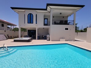 Une maison à deux étages avec une piscine, un espace salon extérieur et une terrasse couverte.
