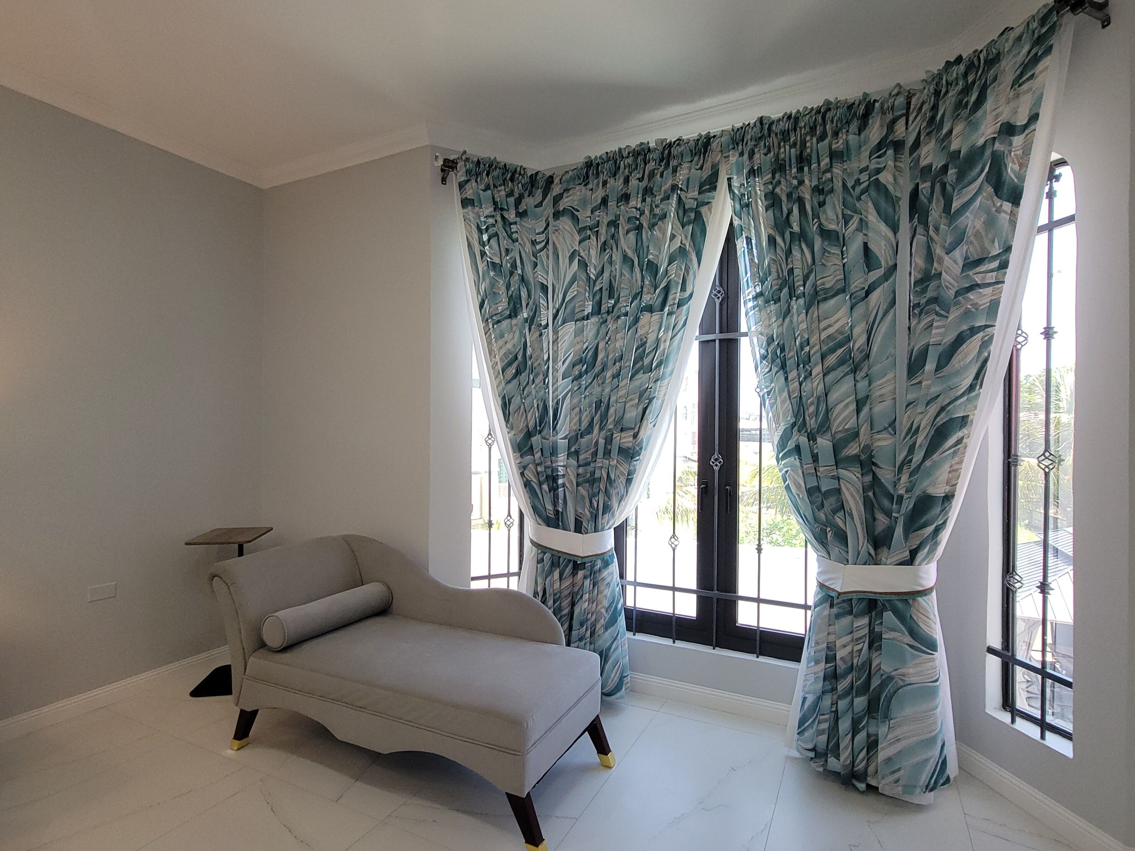 A room with a single sofa, a window with patterned curtains, and a view of the outdoors.