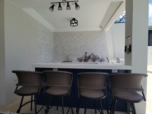 A kitchen with a white countertop, four wicker bar stools, and a hanging light fixture.