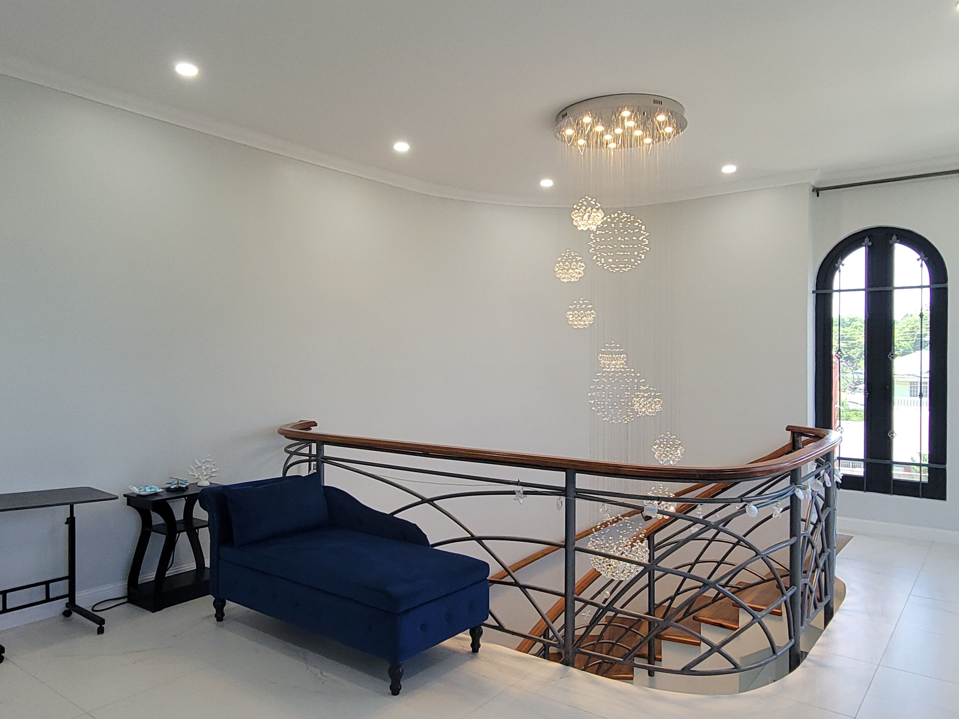 Un intérieur moderne avec un canapé bleu, un escalier doté d’une rampe en métal et un lustre.