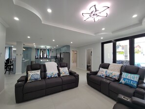 A modern living room with two sofas, a kitchen in the background, and a ceiling fan.