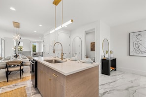 A modern kitchen with a central island, stainless steel sink, and pendant lighting. - Ovation @ The New Cumberland (Nashville)
