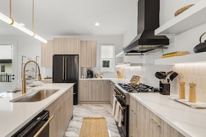 A modern kitchen with a central island, stainless steel appliances, and a built-in oven. - Ovation @ The New Cumberland (Nashville)