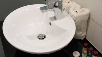 A white bathroom sink with a chrome faucet, a white towel, and toiletries on a black countertop.