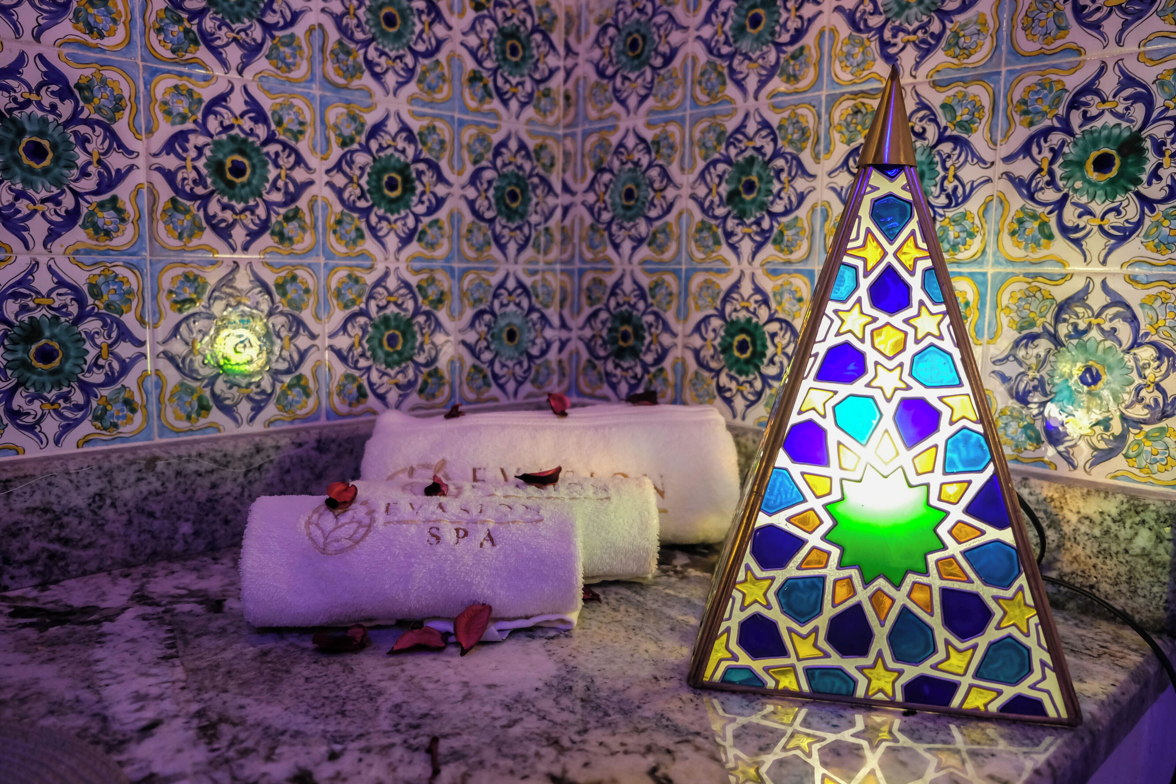 A bathroom with a decorative tiled wall, a towel with 'SPA' written on it, and a stained glass lamp.