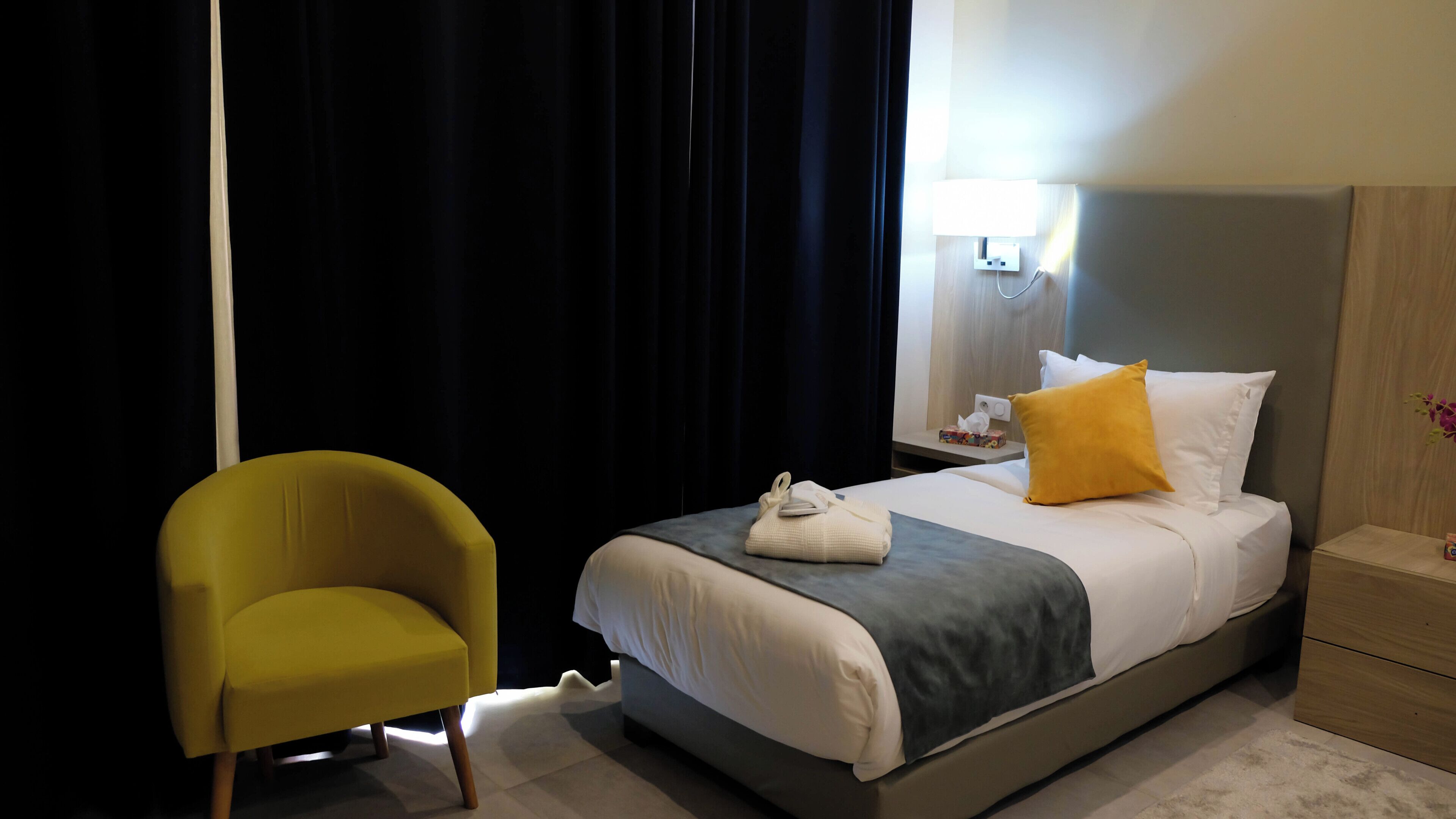 A hotel room with a bed, a nightstand, a lamp, a chair, and a window with curtains.