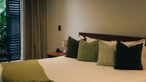 Hotellihuone, jossa on sänky, tyynyjä, yöpöytä, lamppu ja näkymä vihreälle alueelle.