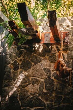 A rustic outdoor setting with a stone floor, a wooden structure with a rustic design, and a hanging rope. - Villa Perezoso - Nuak Jungle (La Palmeria)