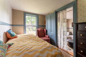 A bedroom with a bed, a chair, a dresser, and a window.