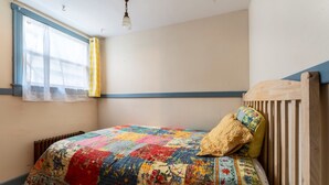 A bedroom with a wooden headboard, a colorful quilt, a radiator, and a window with curtains. - Spacious Harbor Retreat | Easy Access to Downtown (Mount Desert)