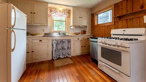 A compact kitchen with white cabinets, a stove, and a refrigerator. - Spacious Harbor Retreat | Easy Access to Downtown (Mount Desert)