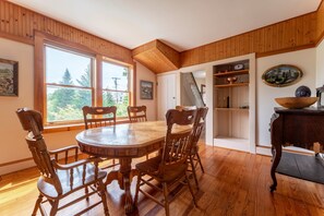 A dining area with a wooden table and chairs, large windows, and a view of greenery outside. - Charming Home Apt - Walk to Acadia & the Harbor (Mount Desert)