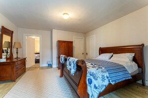 Ein Schlafzimmer mit einem hölzernen Bett, einem Schminktisch, einem Spiegel und einer Tür zu einem weiteren Raum.