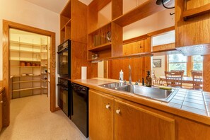 A kitchen with wooden cabinets, a built-in oven, a dishwasher, and a double sink. - Charming Home Apt - Walk to Acadia & the Harbor (Mount Desert)