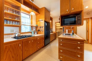 Una cucina con mobili in legno, un frigorifero nero, un forno a microonde e una stufa a gas.