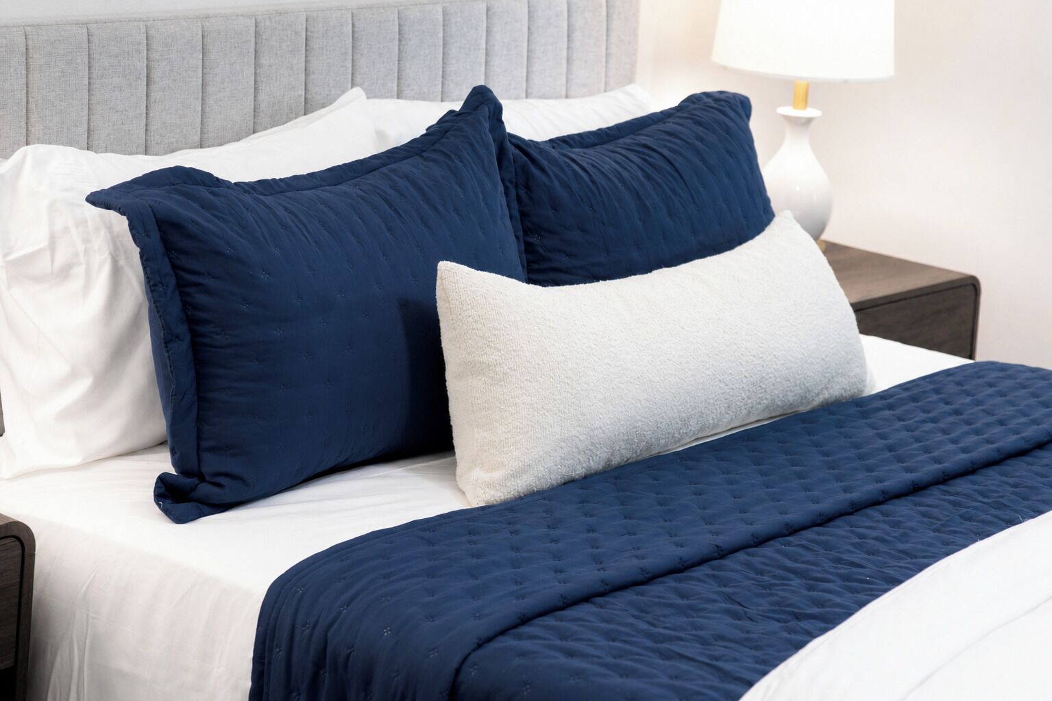 A neatly made bed with a grey headboard, white pillows, and a dark blue quilted bedspread.