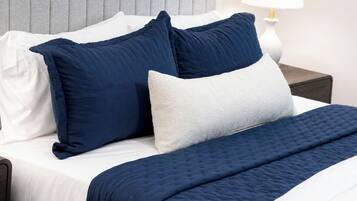 A neatly made bed with a grey headboard, white pillows, and a dark blue quilted bedspread.