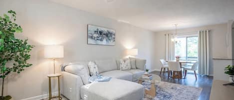 En moderne stue med sofa, skammel og sofabord, et spiseområde med stole, og en loftventilator.
