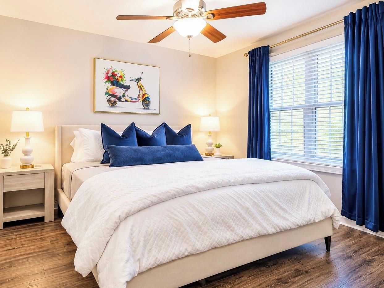 A bedroom with a bed, nightstands, a ceiling fan, a window with curtains, and a wall-mounted picture.
