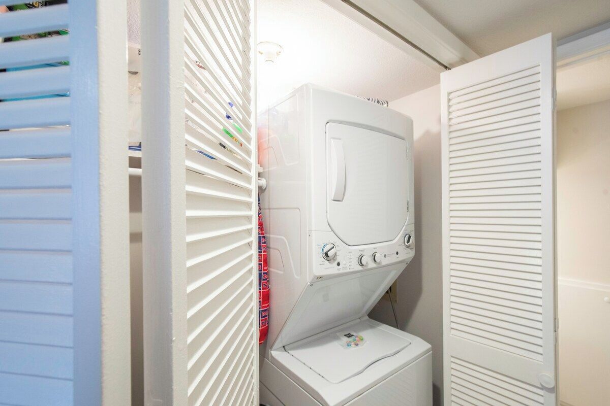A laundry area with a front-loading washer and dryer, a white door, and a window with blinds.