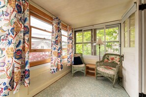 Ein Wintergarten mit Korbmöbeln, einem kleinen Tisch und Blick auf ein Haus durch die Fenster.