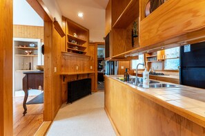 A kitchen with wooden cabinetry, a central island with a sink, and a view into the dining area. - Full Lovely Home Walking Distance to Town & Harbor (Mount Desert)