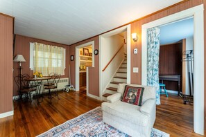A living room with a sofa, a dining table with chairs, a staircase, and a kitchen area. - Full Lovely Home Walking Distance to Town & Harbor (Mount Desert)