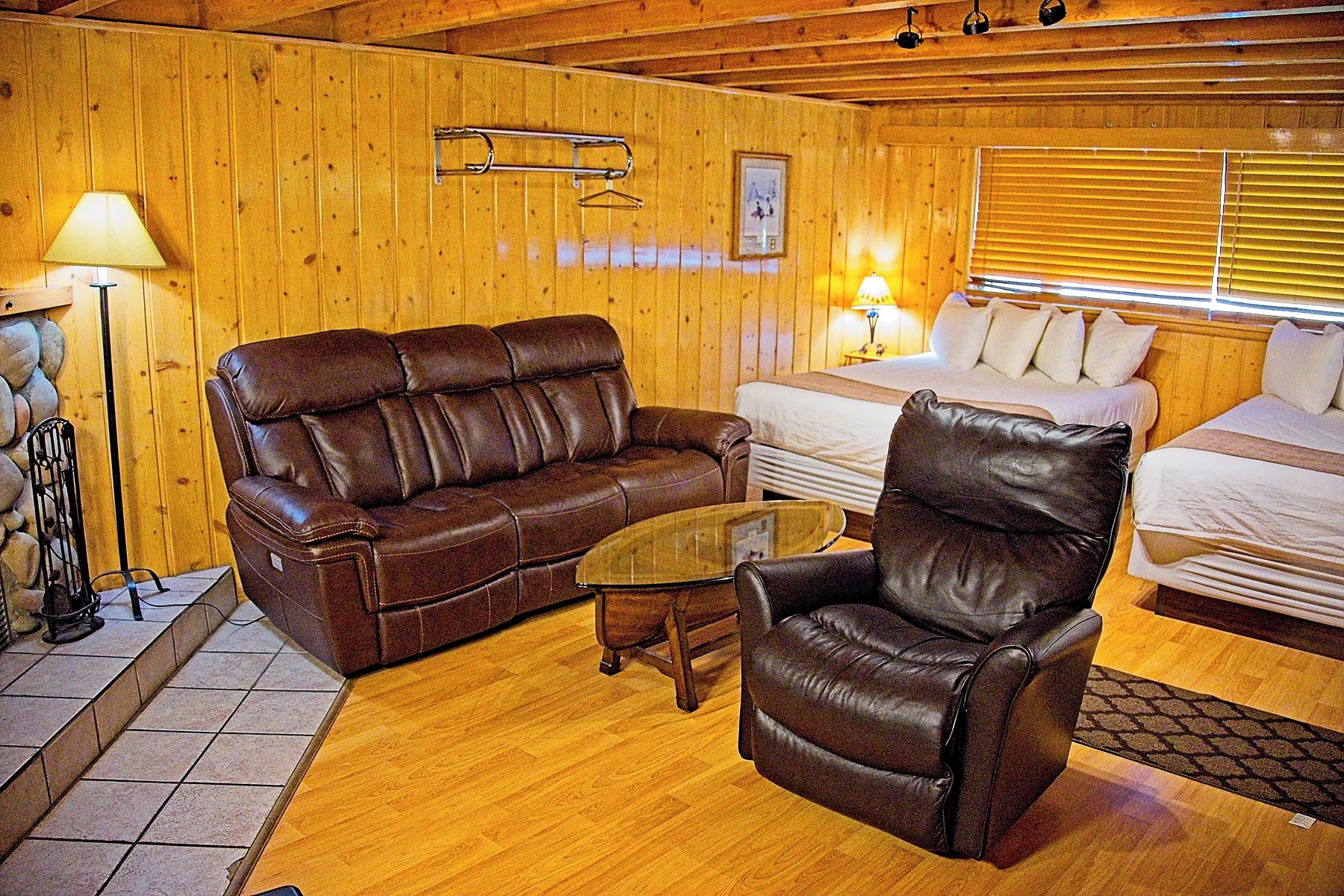 Een kamer met houten lambrisering, een bruine leren bank, een leren fauteuil, een glazen bijzettafeltje en een bed met witte lakens.
