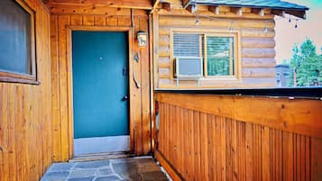 Uma cabana de madeira com entrada de pedra, uma porta azul e uma janela com grade de metal.