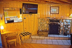 Un intérieur en bois avec une cheminée, un téléviseur fixé au mur et une fenêtre avec des stores.