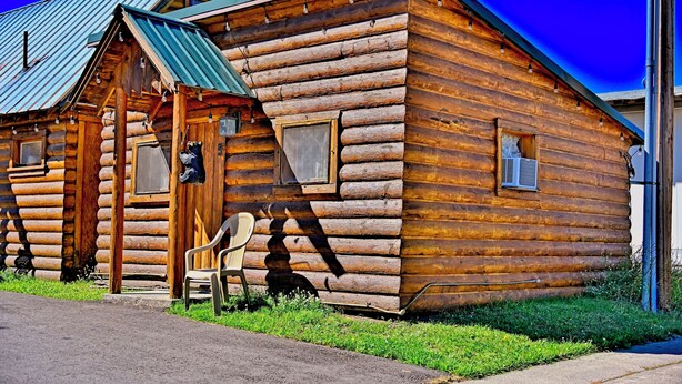 A log cabin with a porch, a chair, and a small table.