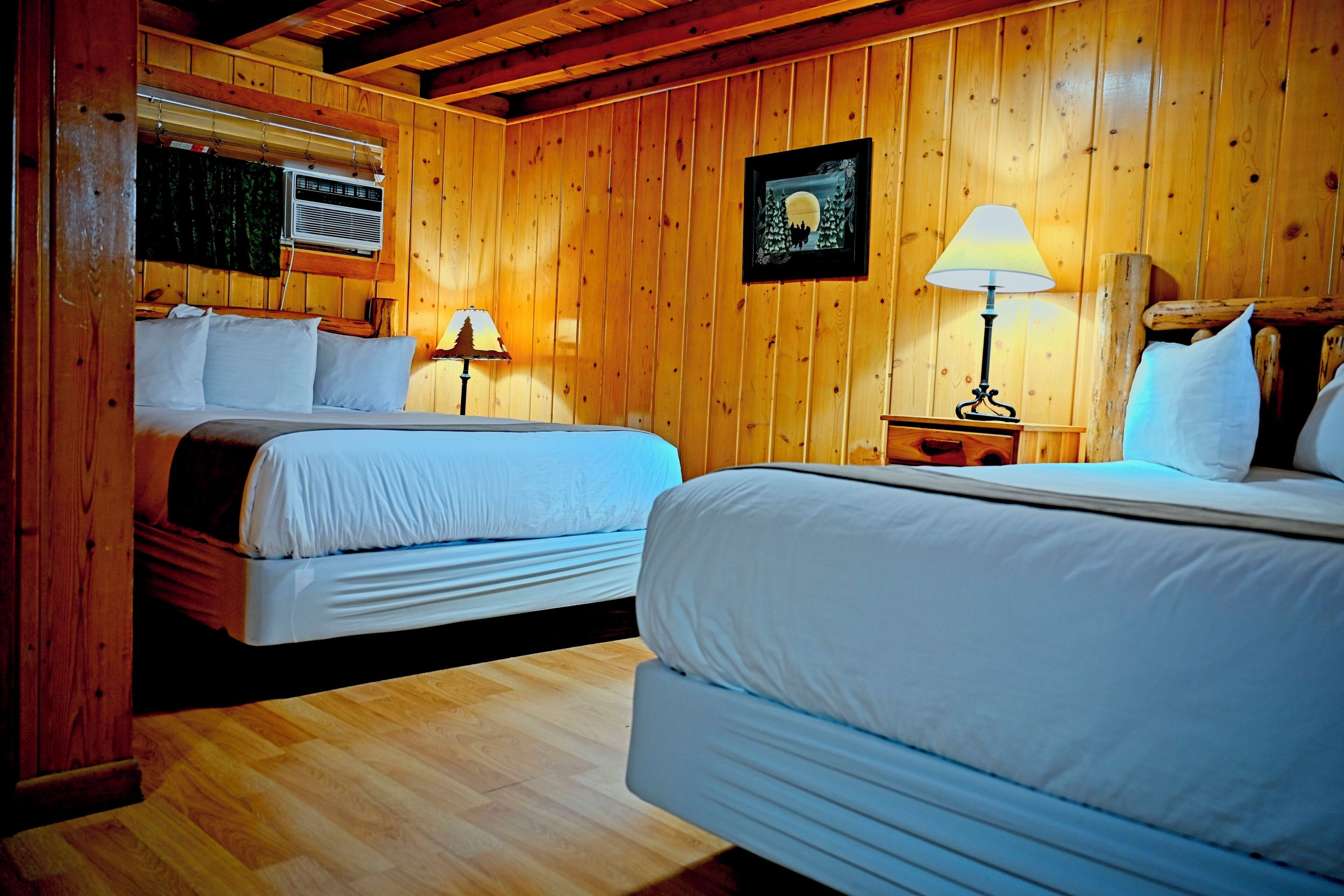 Una habitación de madera con dos camas, una mesita de noche, una lámpara y un cuadro en la pared.