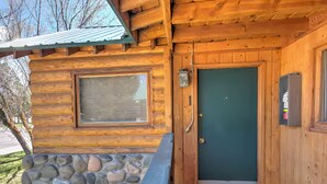 A log cabin with a stone foundation, a green door, and a window.
