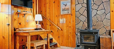A wooden interior with a stone wall, a television mounted on the wall, a table with a lamp, and a fireplace with a chimney.