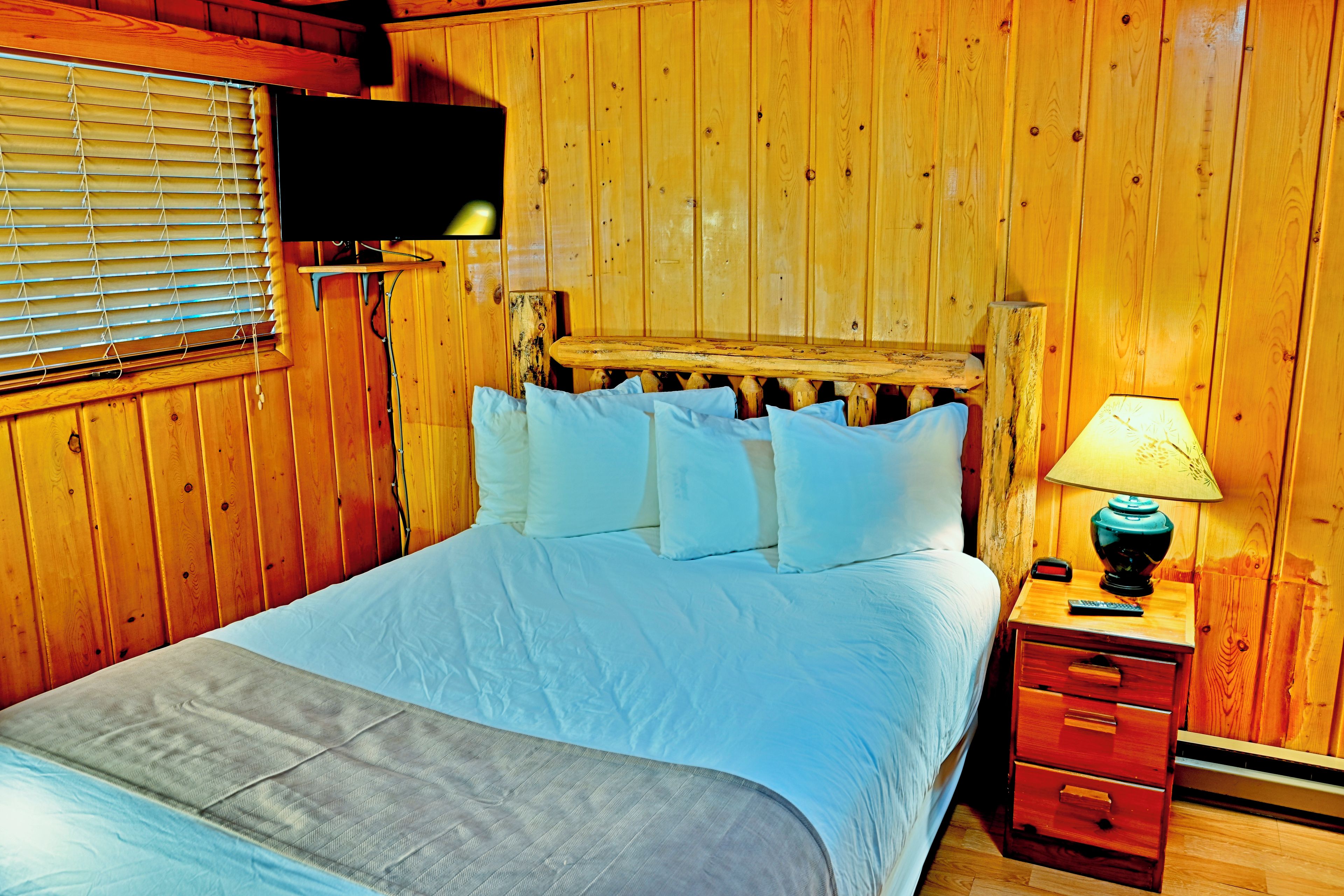 A wooden room with a bed, a nightstand, and a television mounted on the wall.