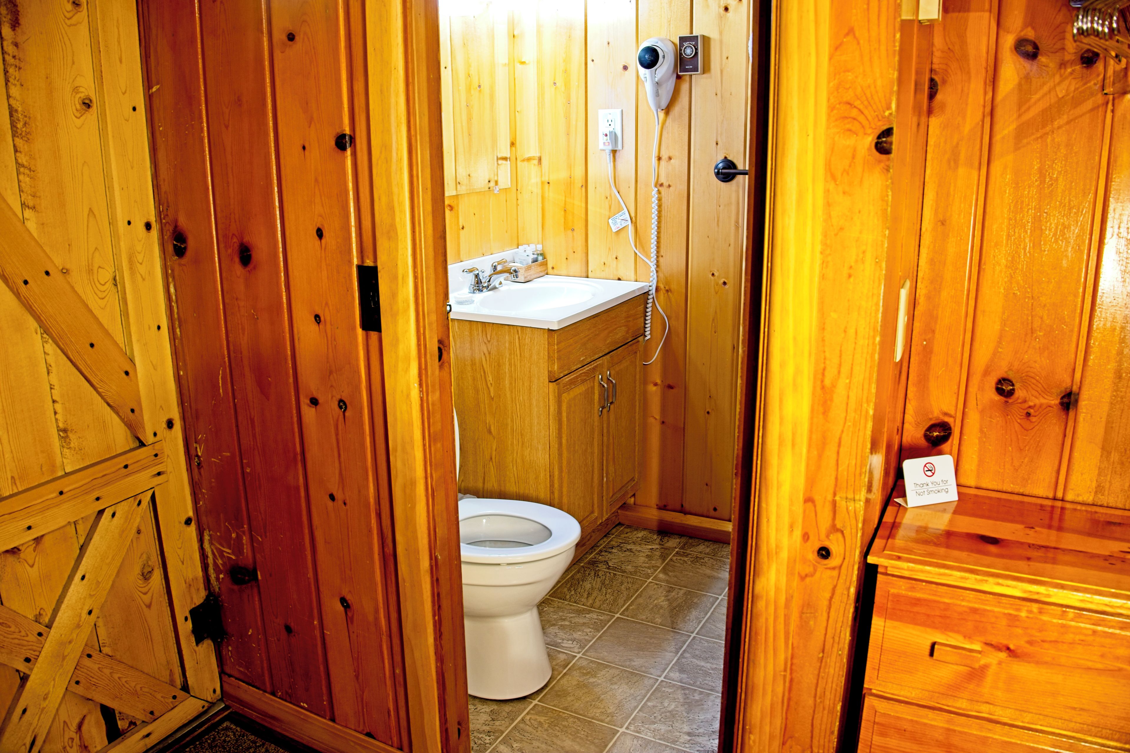 A wooden bathroom with a toilet, sink, and a hairdryer on the wall.