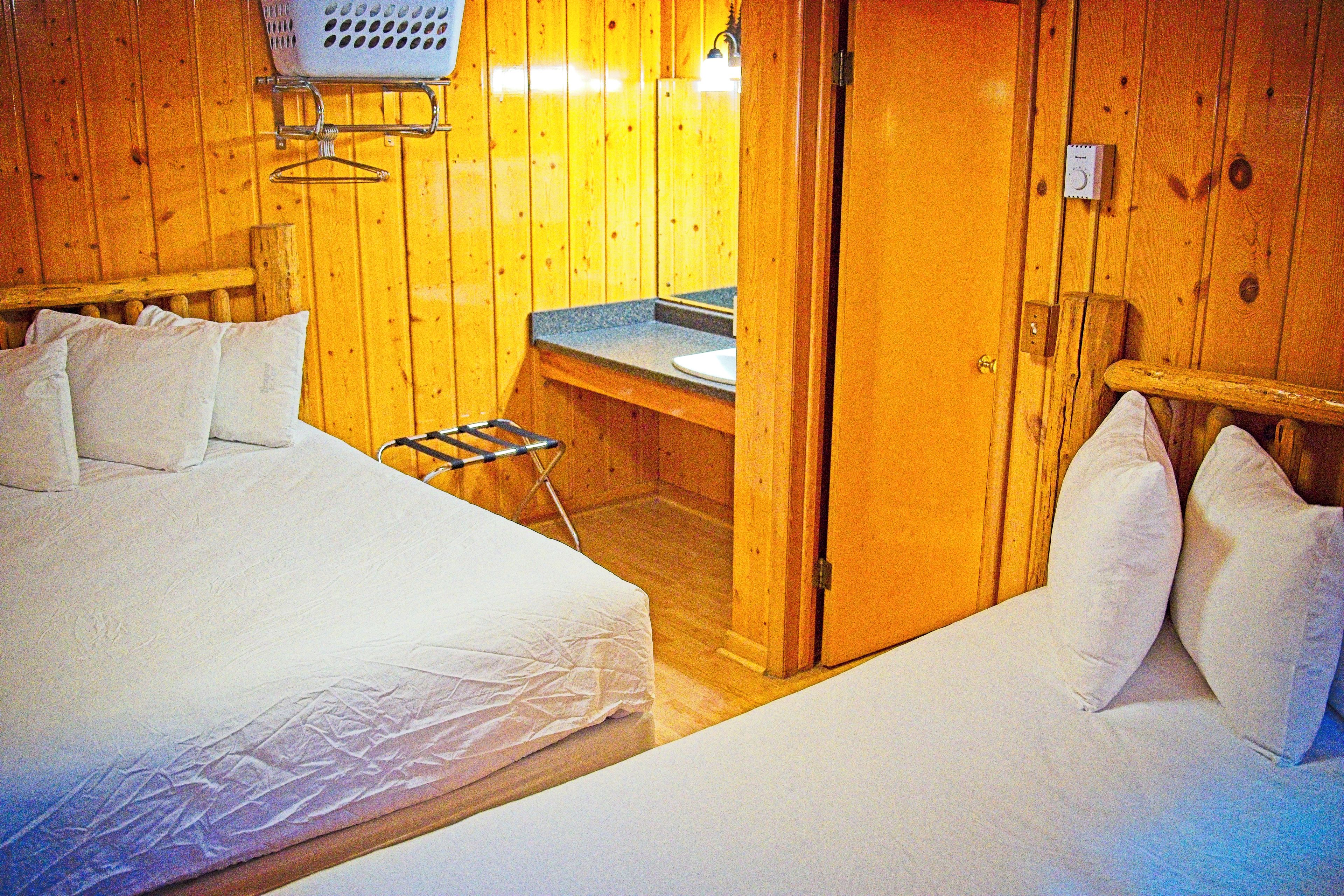 A wooden cabin room with two beds, a small kitchenette, and a wooden door.