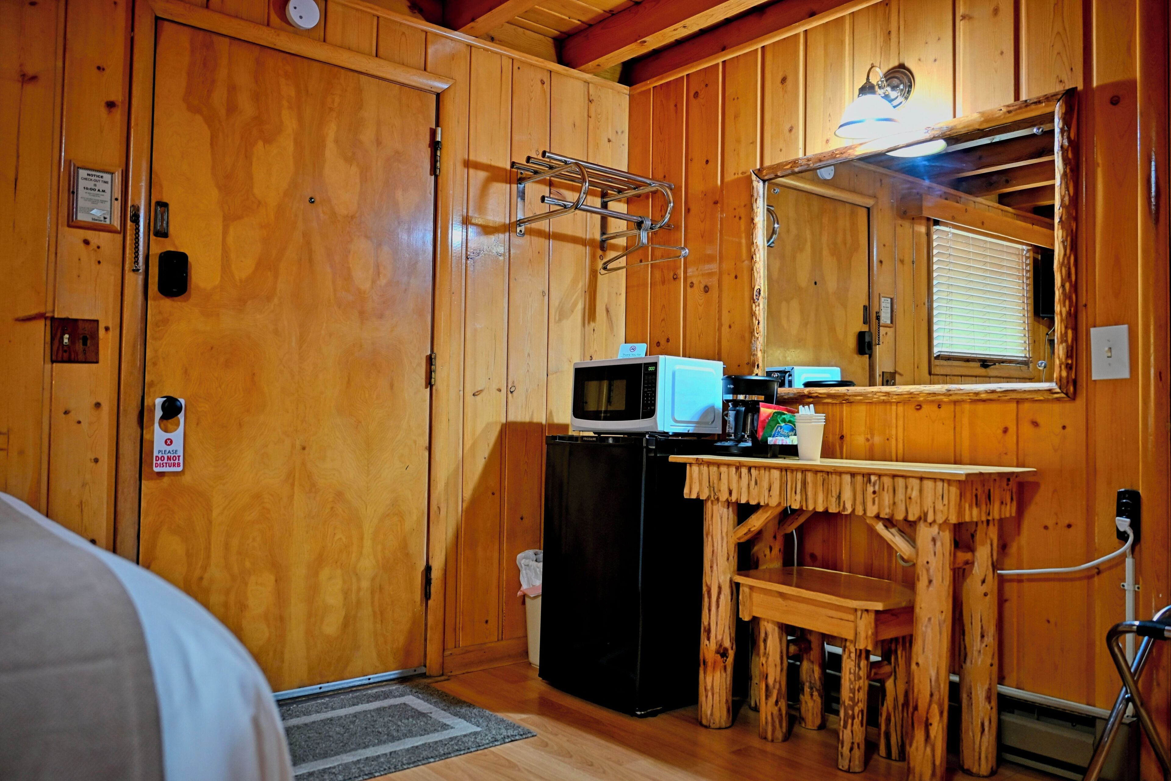 A wooden cabin interior with a kitchenette, a microwave, a small refrigerator, a wooden table, and a chair.