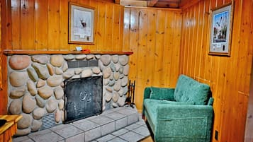 Une pièce avec une cheminée en pierre, un canapé vert, des murs en bois et des tableaux encadrés accrochés au mur.
